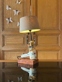 a lamp sitting on top of a wooden table next to a wall with butterflies flying around it