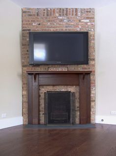 a flat screen tv mounted on top of a brick fireplace in an empty living room