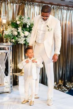 a man in a white suit standing next to a little boy