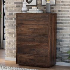 a wooden chest of drawers in front of a brick wall with two pictures on it