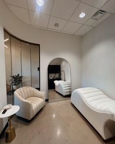 a living room filled with white furniture next to a mirror on the wall and ceiling