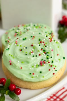 a green frosted cookie with sprinkles on a plate next to holly