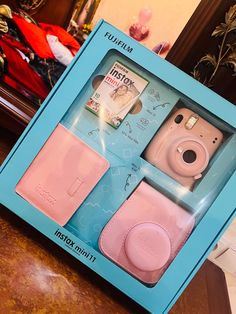 a pink camera and case in a blue box on a wooden table next to a mirror