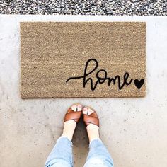 a person standing in front of a door mat with the word home written on it