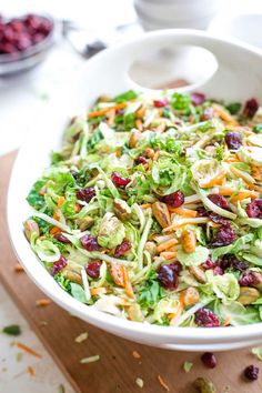 a salad with cranberries and lettuce in a white bowl on a cutting board