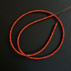 an orange beaded necklace is laying on a black leather surface with a red thread