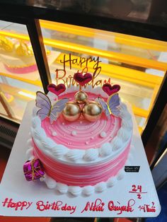 a pink and white birthday cake sitting on top of a table