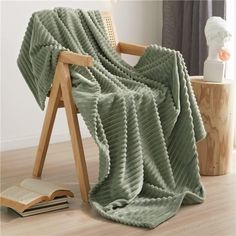 a green blanket sitting on top of a wooden chair next to a book and vase