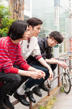 three young men are sitting on a bench