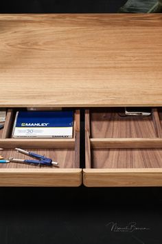 a wooden desk with two drawers holding pens and books