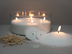 two white candles sitting next to each other on top of a table with some straw in front of them