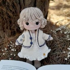 a crocheted doll holding an open book in front of a tree and grass