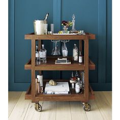 a wooden bar cart with liquor bottles and glasses on the top, in front of a black wall