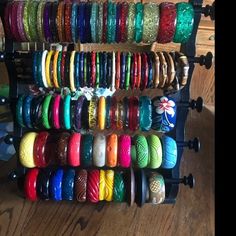 a rack filled with lots of colorful bracelets on top of a wooden floor next to a window