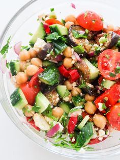 a salad in a glass bowl with tomatoes, cucumbers and chickpeas