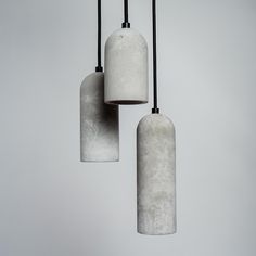 three cement lamps hanging from black cords against a gray background with no one in the photo