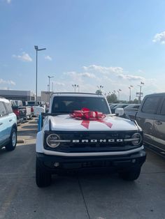 a white truck with a red bow on it's hood parked in a parking lot