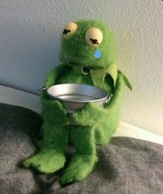 a green stuffed animal holding a metal bowl