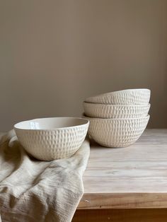 two white bowls sitting on top of a wooden table next to a cloth covered bowl