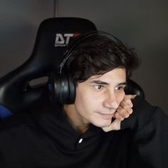 a young man wearing headphones while sitting in front of a computer monitor with his hand on his chin