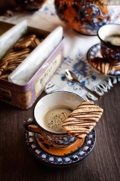 there is a cup of coffee on the table with crackers and cookies in front of it