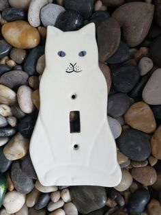 a white cat light switch cover sitting on some rocks