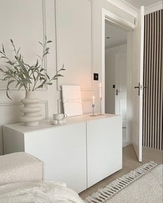 a room with white furniture and a plant on top of the cabinet next to it