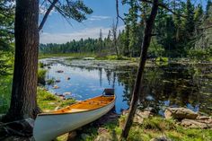 a canoe sitting on the shore of a lake near some trees and rocks in the grass