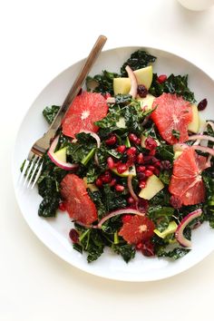 a white plate topped with greens and fruit next to a glass of watermelon