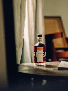 a bottle of rum sitting on top of a wooden table next to a book and chair