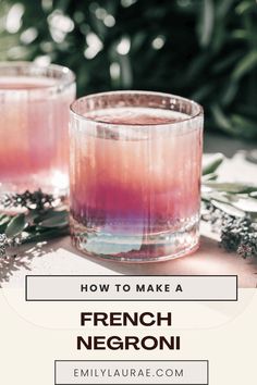 two glasses filled with pink liquid sitting on top of a table next to greenery