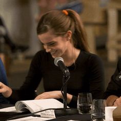 two people sitting at a table with microphones in front of them and papers on the table