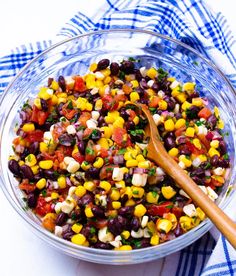 a glass bowl filled with black beans, corn and cilantro on top of a blue checkered table cloth