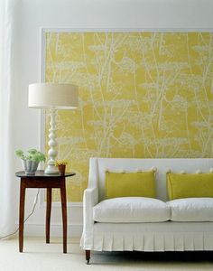 a white couch sitting in front of a yellow wall with trees on it's side