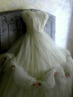 a white dress with pink flowers on it sitting on top of a wooden chair in front of a window