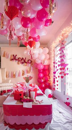 a room filled with lots of pink and white balloons hanging from the ceiling next to a table