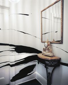 a mirror sitting on top of a wooden table next to a wall with black and white paint