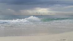 waves crashing on the beach with dark clouds in the sky over the ocean and an island in the distance