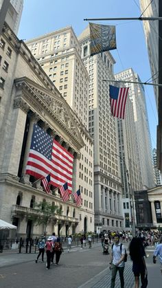 people walking down the street in front of tall buildings with american flags hanging from them