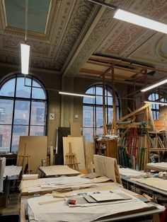 an art studio with large windows and lots of work on the desks in front of them