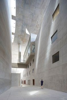 a person standing in an empty building with concrete walls and windows on either side of the room