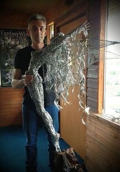 a man is holding up a sculpture made out of silver wire and plastic wrappers