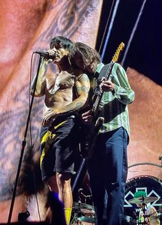 two shirtless men on stage with guitars