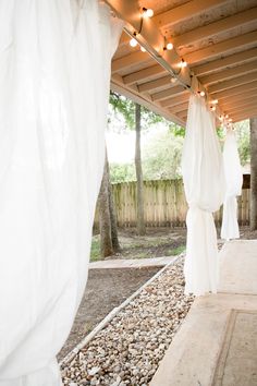 an outdoor covered patio with lights strung from the ceiling and curtains draped over it's sides