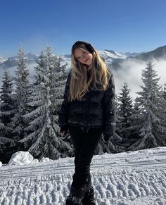 a woman standing on top of a snow covered slope with trees in the back ground