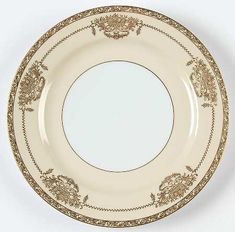 a white and gold plate with an ornate design on the rim, against a white background