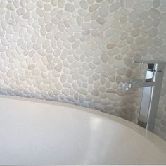 a white bath tub sitting under a faucet next to a wall covered in rocks