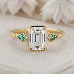 an emerald and diamond engagement ring on a white cloth with feathers in the back ground