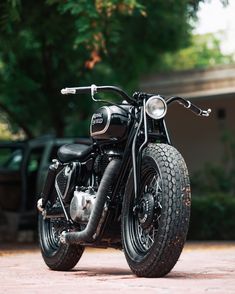 a black motorcycle parked on top of a brick road next to a green tree filled forest