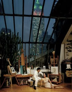 a man and woman sitting on the floor in front of a window with a city skyline behind them